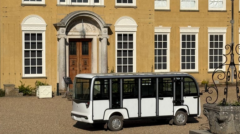 A white shuttle bus is parked outside the main house at Polesden Lacey